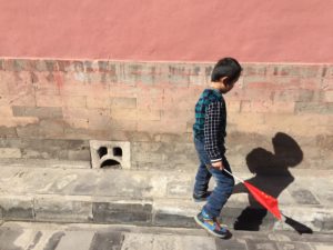 A young boy holding a Chinese flag walking on a sun-bathed sidewalk