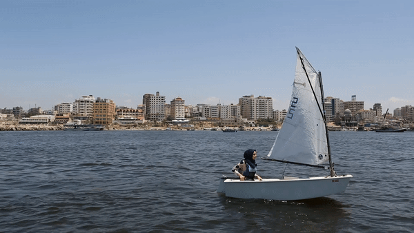 A gif of a young girl sailing on the ocean, a skyline of gaza behind her