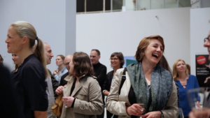 A screenshot from the video showing a group of people in a gallery, laughing